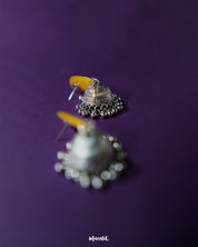 Detailed view of Gulrukh floral jhumkas, highlighting the painted yellow-red motif and intricately carved oxidized silver dome against a plain backdrop – Muselot.