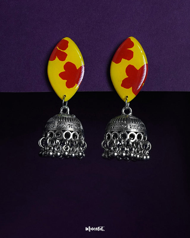 Gulrukh red floral jhumkas with yellow marquise tops and oxidized silver dome drops, displayed against a purple backdrop to highlight their bold traditional charm – Muselot.