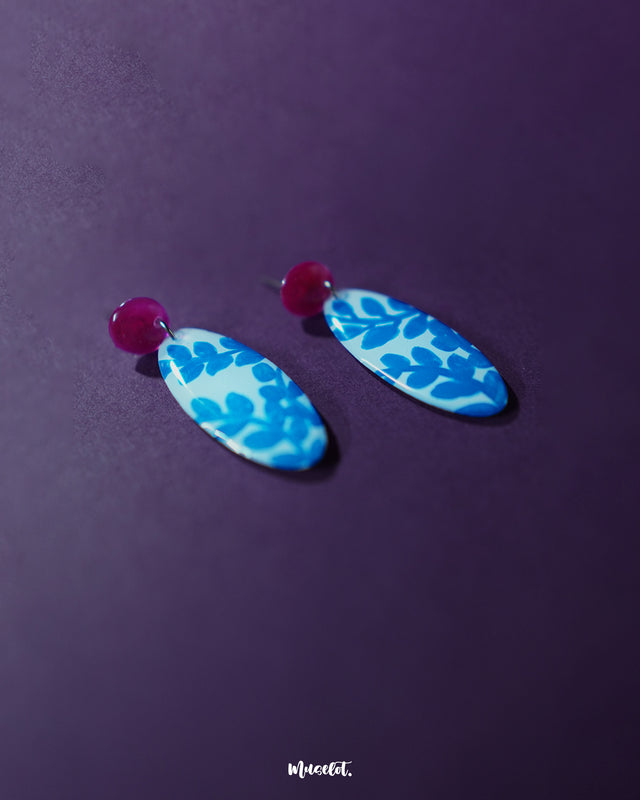 Gulsaba blue handmade drop earrings featuring glossy red circular studs connected to elongated white oval drops adorned with bold hand-painted blue leafy patterns, beautifully showcased to highlight their artistic and vibrant design – Muselot.