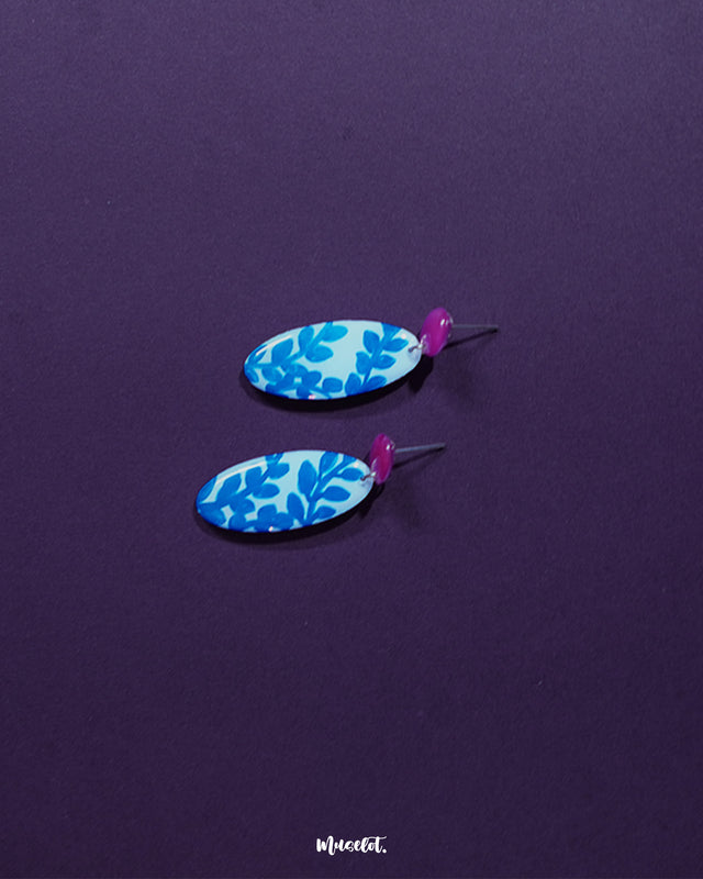 Gulsaba blue handmade drop earrings with glossy red circular studs and elongated white oval drops decorated with striking hand-painted blue leafy patterns, elegantly displayed to emphasize their bold and contemporary craftsmanship – Muselot.