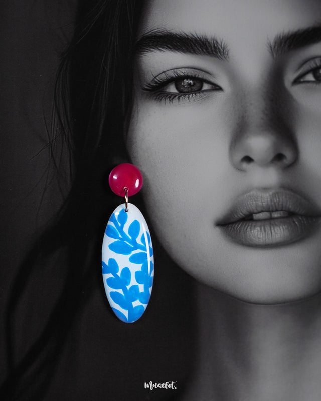 Close-up of model wearing the Gulsaba drop earrings, showcasing glossy red circular studs paired with elongated oval drops in white decorated with hand-painted blue leafy patterns, highlighting their bold and artistic design – Muselot.