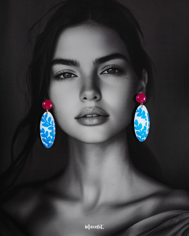 Model wearing the Gulsaba drop earrings, featuring glossy red circular studs with elongated oval drops in white adorned with hand-painted blue leafy patterns, elegantly highlighting their vibrant and contemporary style – Muselot.