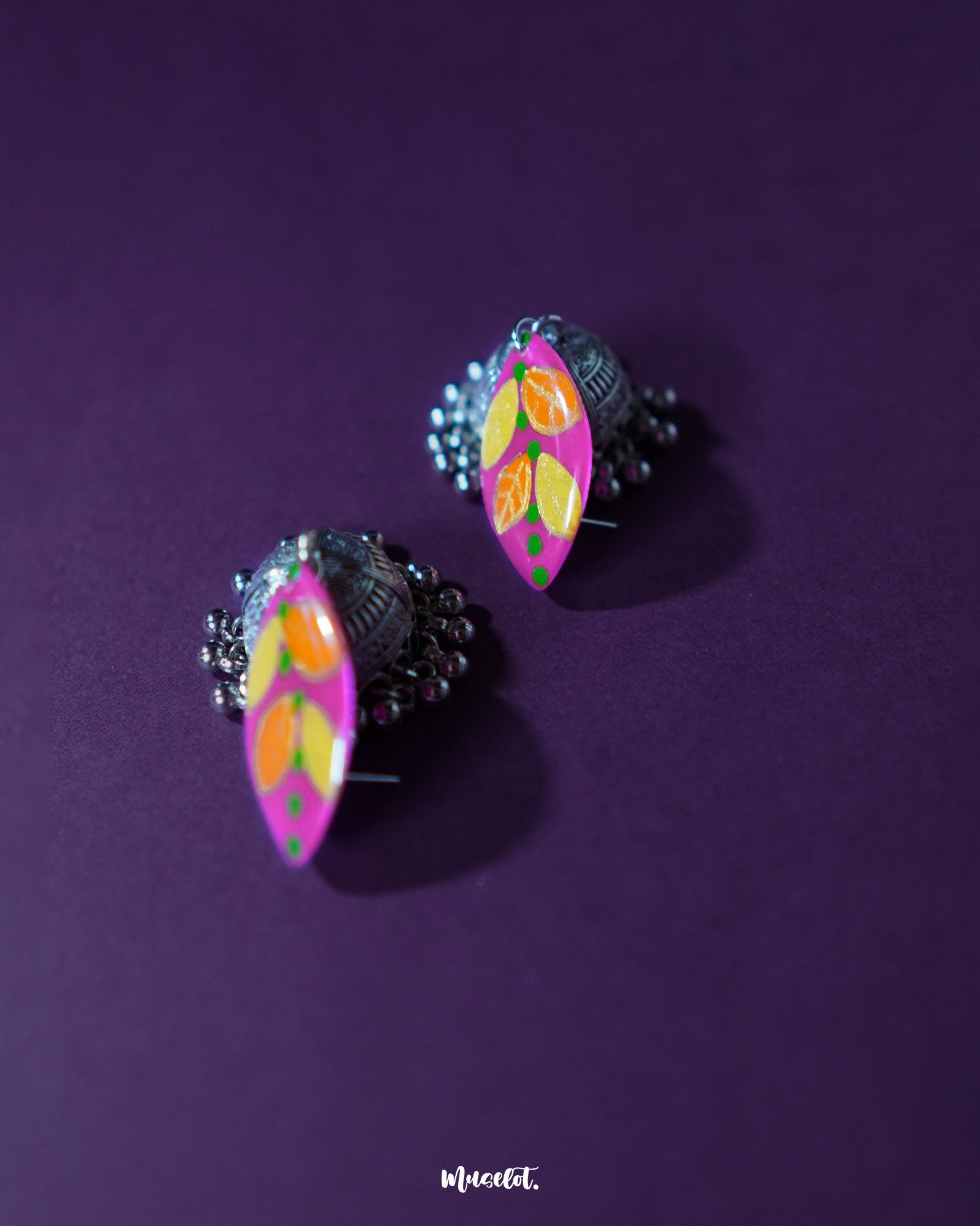Top view of the upper part of the Gulzarish floral jhumkas, showcasing the marquise-shaped purple tops adorned with orange and yellow leaf motifs accented by green dots, highlighting the vibrant colors and intricate hand-painted detailing – Muselot.