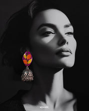 Model wearing the Gulzarish jhumkas, showcasing marquise-shaped purple tops with orange and yellow leaf motifs accented by green dots, paired with intricately carved oxidized silver dome-shaped jhumka drops with delicate hanging beads, highlighting their vibrant and traditional charm – Muselot.
