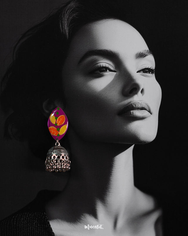 Model wearing the Gulzarish jhumkas, showcasing marquise-shaped purple tops with orange and yellow leaf motifs accented by green dots, paired with intricately carved oxidized silver dome-shaped jhumka drops with delicate hanging beads, highlighting their vibrant and traditional charm – Muselot.