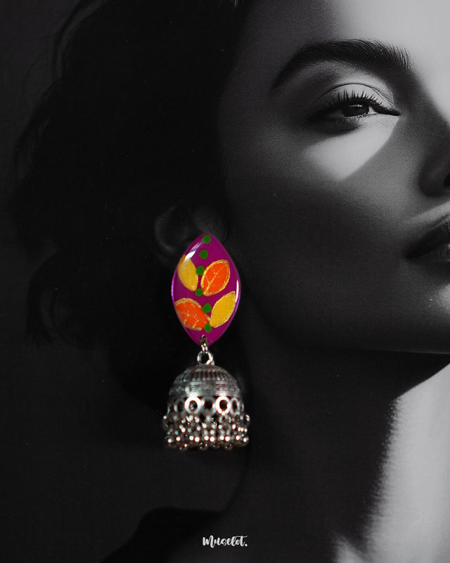Close-up of model wearing the Gulzarish jhumkas, featuring marquise-shaped purple tops with orange and yellow leaf motifs accented by green dots, paired with ornate oxidized silver dome-shaped jhumka drops adorned with delicate hanging beads, capturing their intricate detailing and vibrant design – Muselot.