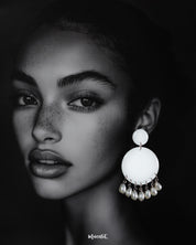 A woman wearing the handmade Noor stud drop earrings, featuring white circular studs with hanging pearl drops, showcasing the timeless grace and subtle charm of artisan-crafted elegance — Muselot.