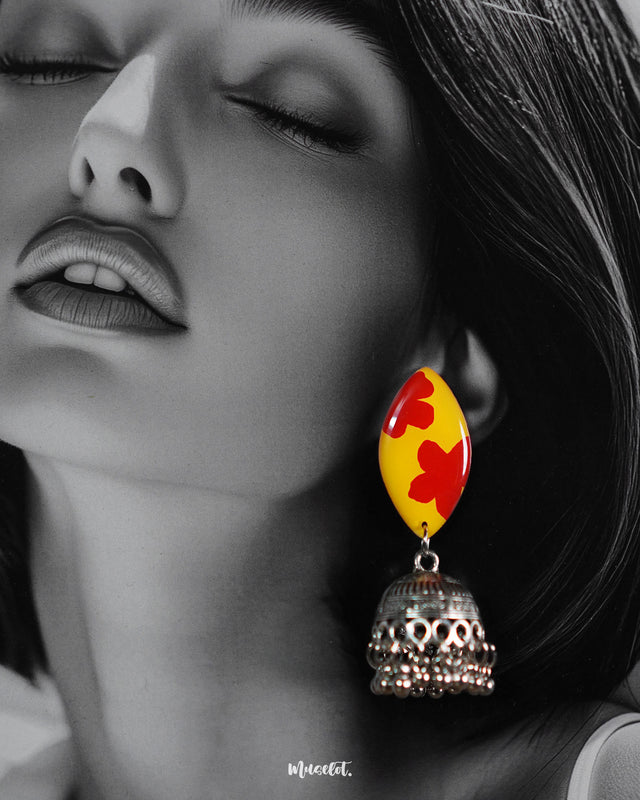 Close-up of model wearing hand-painted floral jhumkas, featuring a bold yellow-red motif with oxidized silver drops, highlighting the detailed craftsmanship – Muselot.