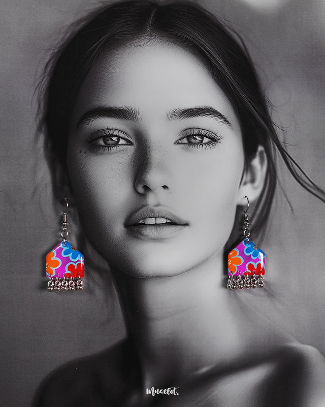 Model wearing hand-painted hook earrings with colourful floral motifs and silver ghungroo drops, highlighting their playful bohemian charm – Muselot.
