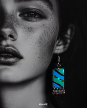 A woman wearing the Jaltarang boho drop earrings shows off their intricate hand-painted aqua detailing and dangling silver elements, capturing a free-spirited, earthy elegance—Muselot.