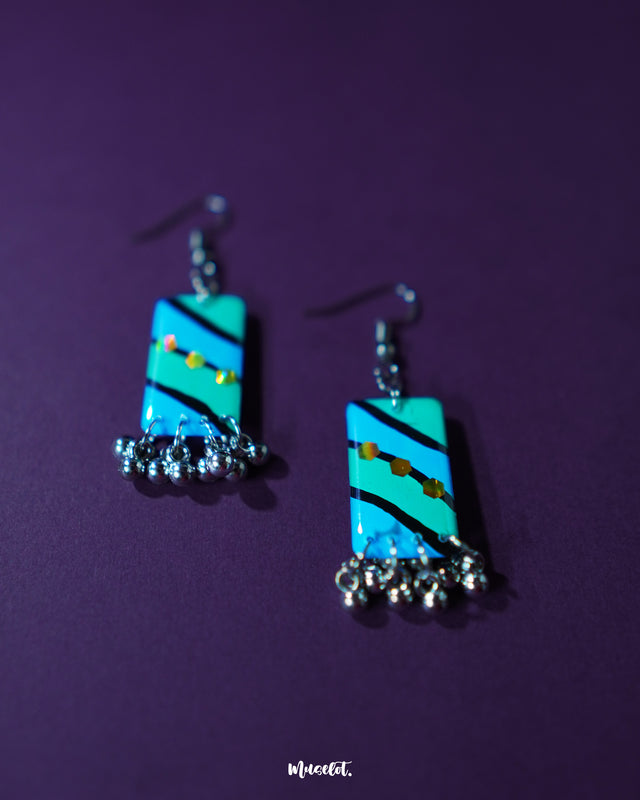 A pair of Jaltarang handmade strip hook earrings is displayed on a textured background, highlighting their airy construction and fluid strip design that speaks to artisanal craftsmanship and minimalist charm — Muselot.