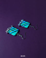 A pair of Jaltarang square strip earrings displayed on a textured white backdrop, highlighting the sharp geometry of the square top and the rhythmic flow of the dangling silver strips — Muselot.