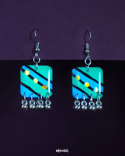 A pair of Jaltarang strip drop earrings featuring hand-painted in vivid green and blue diagonal stripes, adorned with yellow dot motifs and finished with silver-toned ghungroos that add a soft jingle—Muselot.
