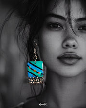 A woman wears the Jaltarang strip drop earrings, their hand-painted green and blue stripes standing out vividly against her skin, while the silver ghungroos at the bottom add a rhythmic charm to her look—Muselot.