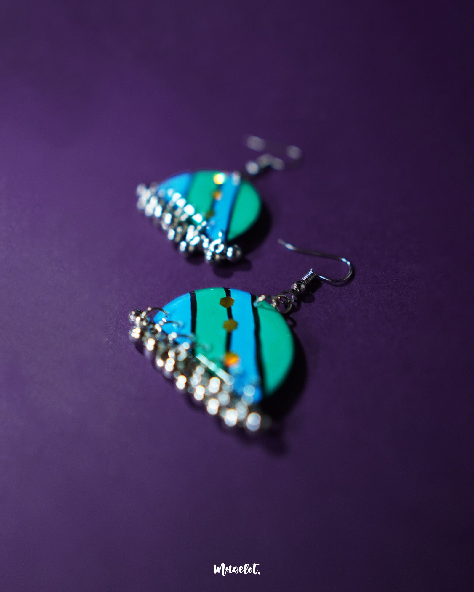 Jaltarang strip earrings displayed against a rich purple background, showcasing their elegant linear design with a glossy, oceanic shimmer—Muselot.