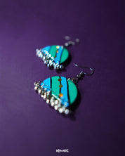 Jaltarang strip earrings displayed against a rich purple background, showcasing their elegant linear design with a glossy, oceanic shimmer—Muselot.