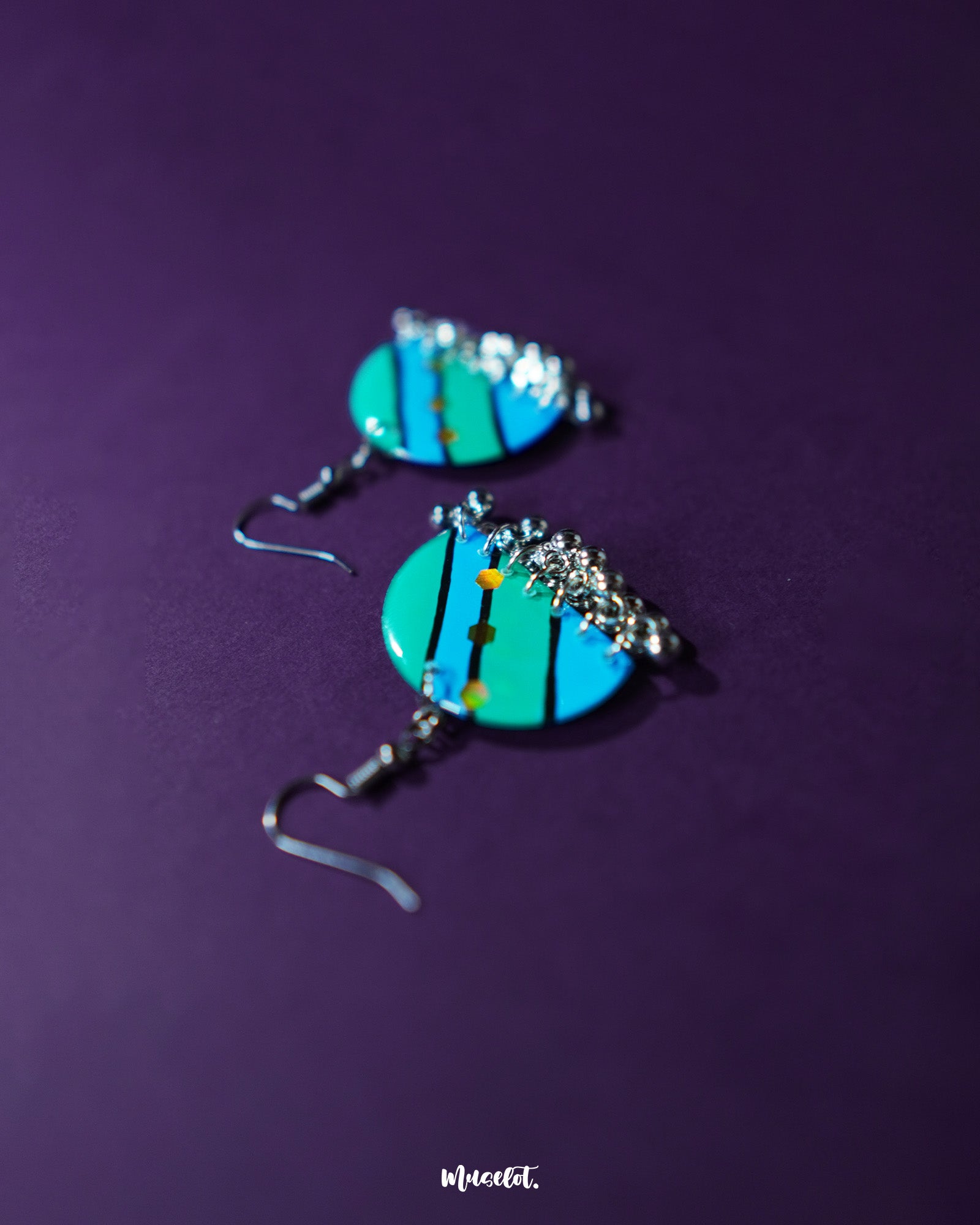 A pair of Jaltarang strip earrings displayed against a soft purple background, featuring sleek vertical lines and subtle metallic sheen that adds a modern yet cultural charm—Muselot.