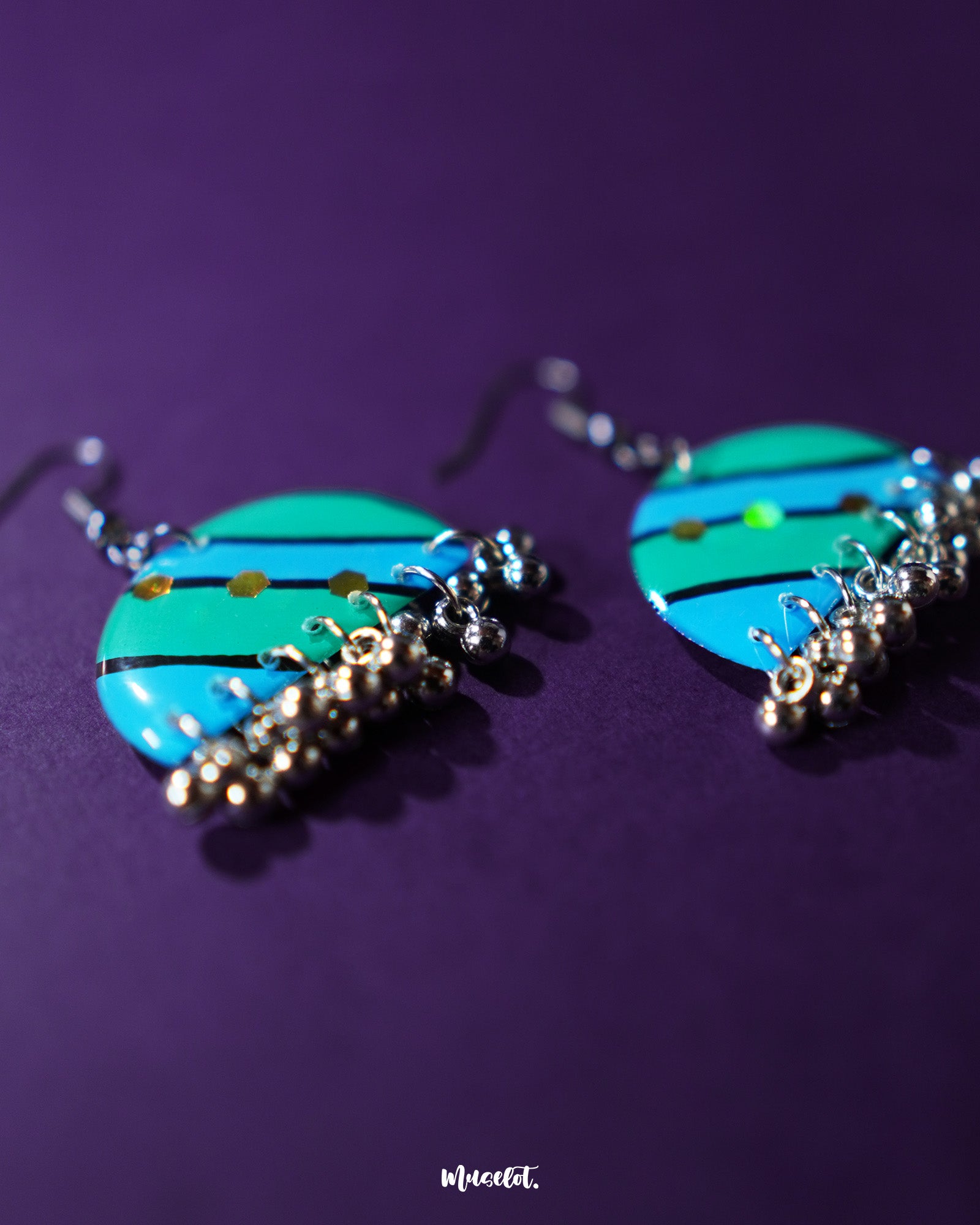 The Jaltarang strip earrings are displayed on a fabric backdrop, highlighting their minimal silhouette and reflective finish that adds a refined charm—Muselot.