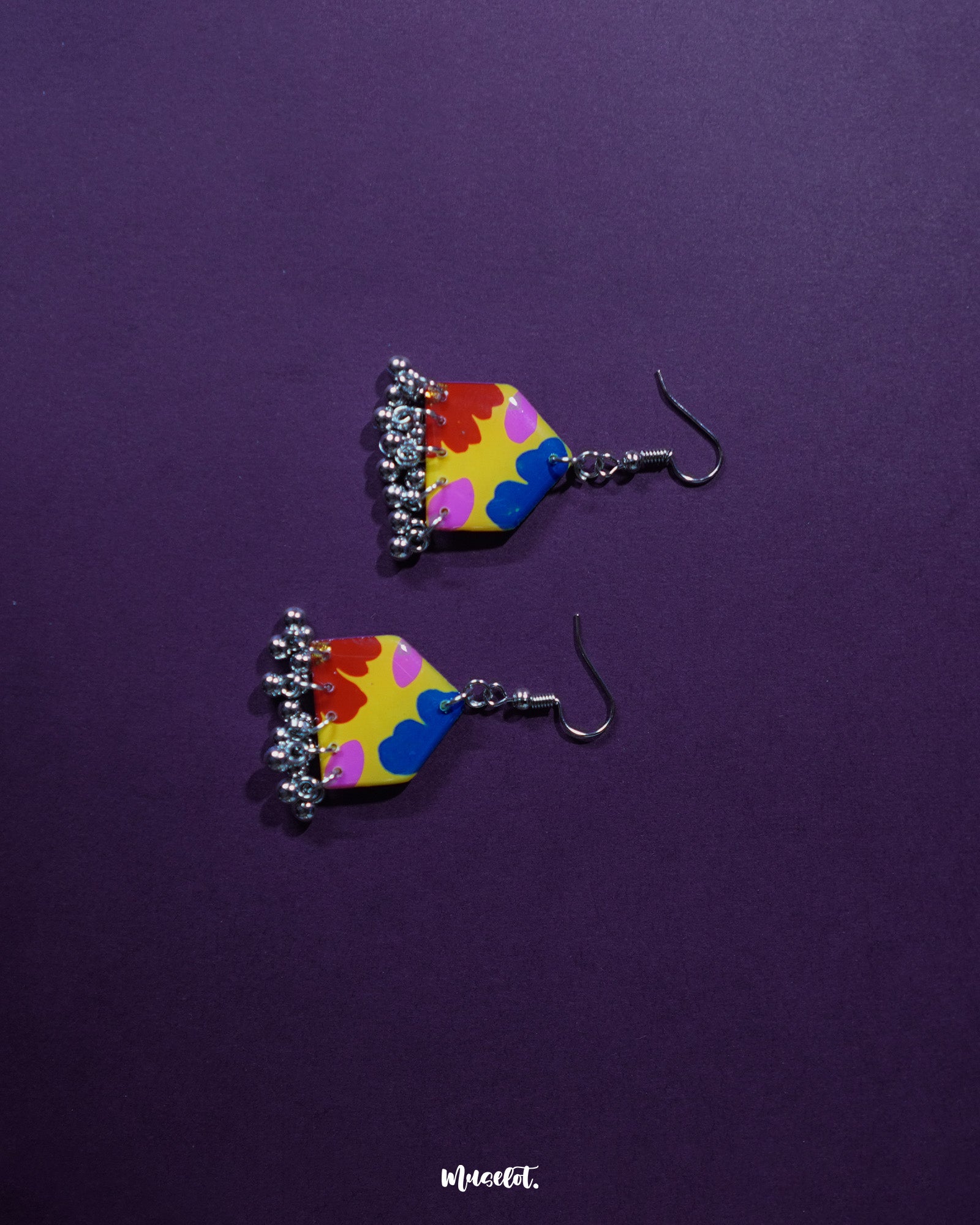 Jharokhe multicolor floral hook earrings placed against a deep purple background, featuring a bold mix of red, yellow, blue, and pink floral patterns with silver ghungroo dangles that highlight their handcrafted vibrance — Muselot.