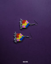 Jharokhe multicolor floral hook earrings placed against a deep purple background, featuring a bold mix of red, yellow, blue, and pink floral patterns with silver ghungroo dangles that highlight their handcrafted vibrance — Muselot.