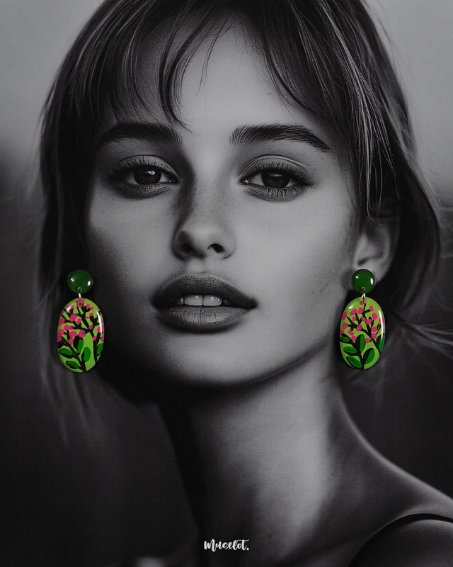 A woman wears the Kalibaan handmade drop earrings, highlighting the playful contrast of lush green and bright pink floral art. The hand-painted design stands out beautifully, showcasing the charm of nature-inspired craftsmanship in a bold and wearable style — Muselot
