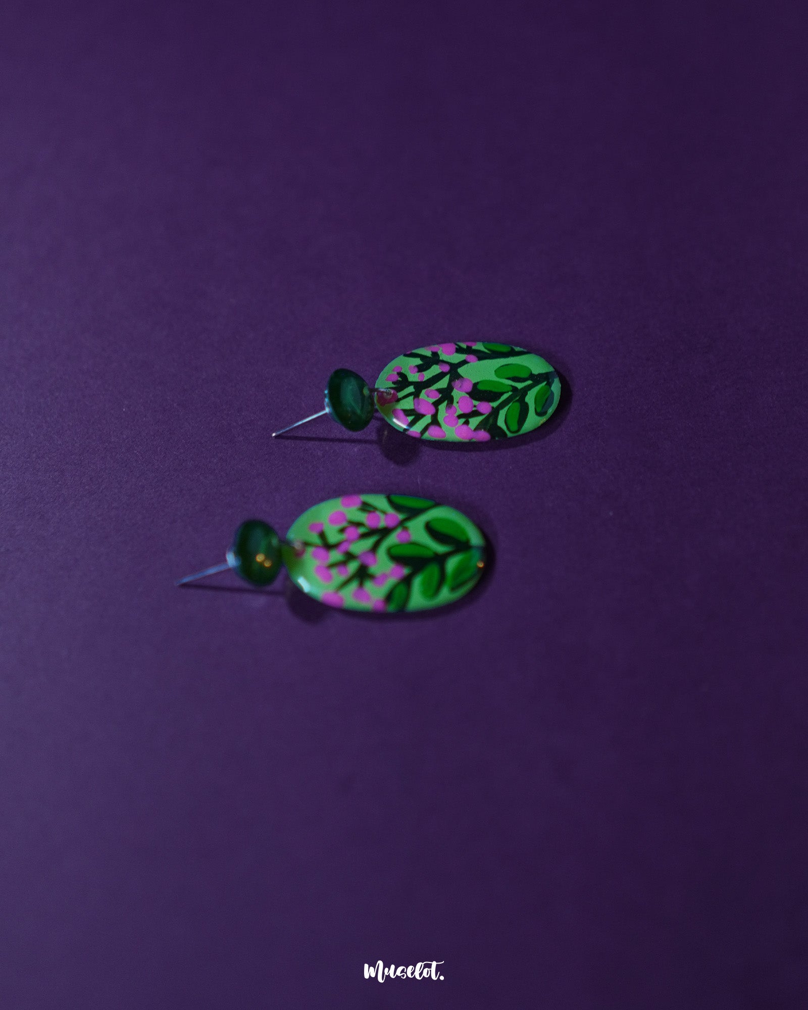 A pair of Kalibaan handmade drop earrings laid flat on a natural backdrop, showcasing the bright floral motifs and oxidized metallic finish. The design highlights bold color contrast and artistic detailing — Muselot.
