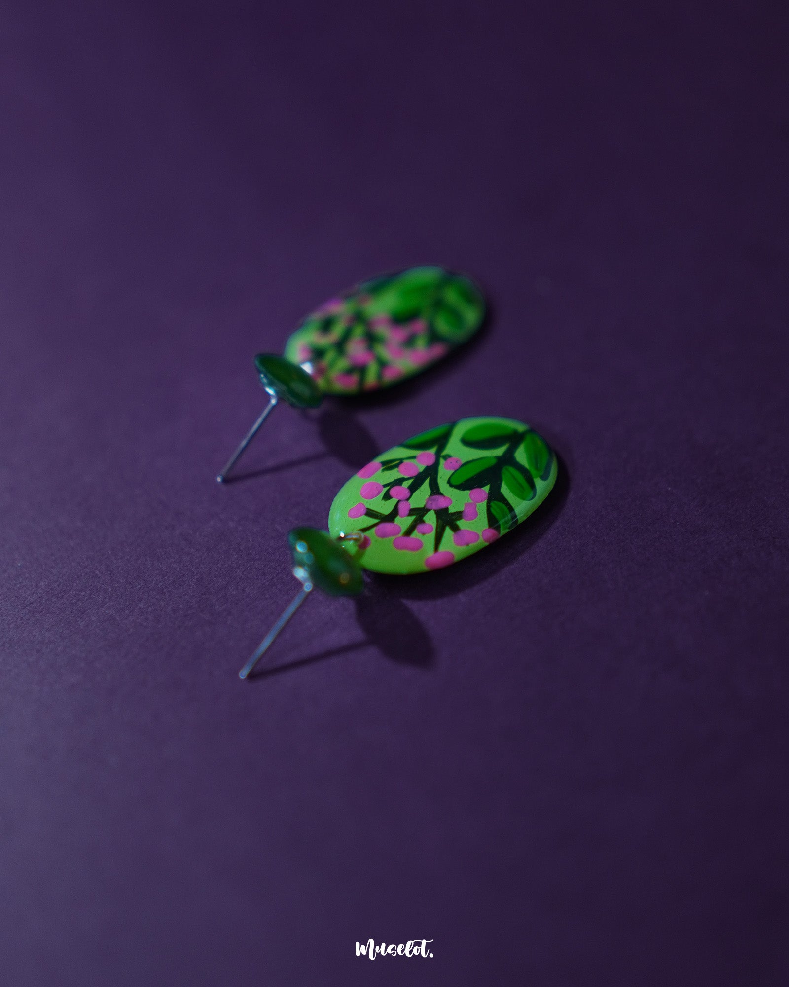 The Kalibaan handmade drop earrings placed against a soft purple background, highlighting the hand-painted floral details and intricate metalwork. The rich contrast showcases the earrings' artistic charm and vibrant elegance — Muselot.