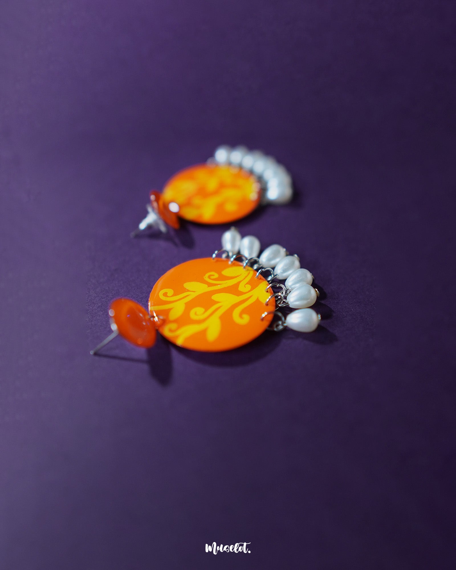 A striking pair of Kesarbaan earrings featuring bold orange and yellow hand-painted patterns, accentuated with dangling white pearls that add a graceful sway – Muselot.