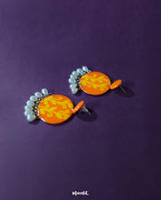 Kesarbaan earrings displayed in a flatlay, highlighting their symmetrical orange and yellow motifs with pearl drop detailing – perfect for adding a handcrafted charm to ethnic or boho looks – Muselot.