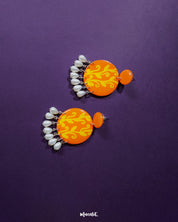 These Kesarbaan orange and yellow drop earrings highlight their unique layered design — vibrant floral accents paired with glistening pearls create a festive, eye-catching look that’s perfect for uplifting any outfit — Muselot.