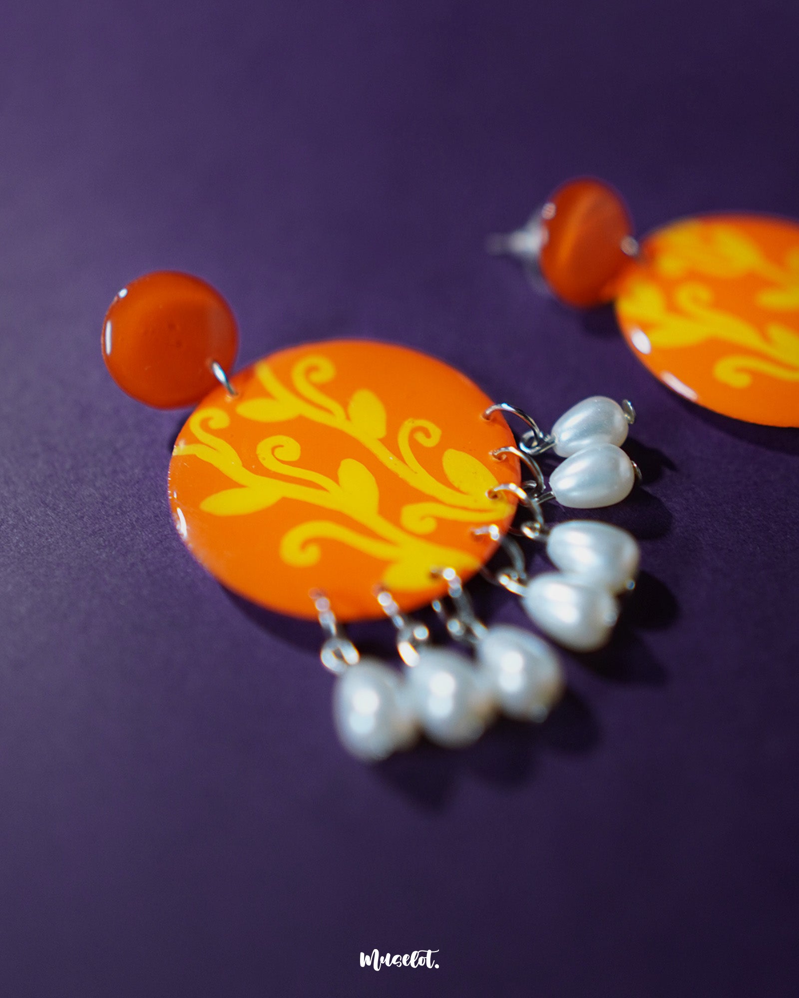The Kesarbaan orange and yellow drop earrings showcase an elegant downward cascade of floral elements with pearl detailing, blending warm tones and intricate craftsmanship for a graceful and festive aesthetic — Muselot.