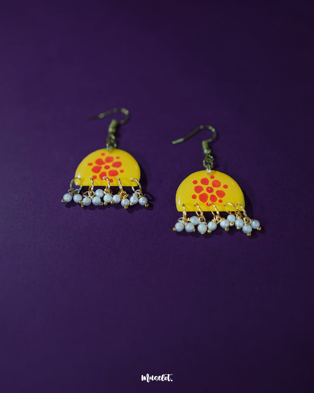 Kesarika floral yellow hook earrings, placed against a deep purple backdrop, featuring bright floral motifs and intricate accents that create a striking balance of boldness and refined beauty — Muselot.