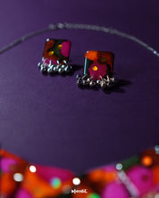 Khushk Gul handmade floral earring featuring a square charm with vibrant pink, orange, and green abstract floral patterns accented by delicate silver beads, beautifully showcased to highlight its intricate design and lively colors – Muselot.