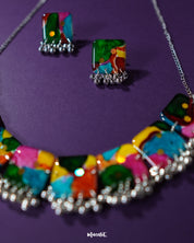 The Kohsar colorful jewelry set laid out on a rich purple backdrop, showcasing its bohemian style with vibrant beads in assorted hues, ornate metal elements, and coordinated earrings — a statement ensemble full of artistic flair — Muselot.