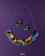 A vibrant multicolor boho necklace set from Muselot, laid out against a deep purple background. The set features bold, beaded detailing with an eclectic mix of colors and textures, highlighting its artistic and statement-making charm — Muselot