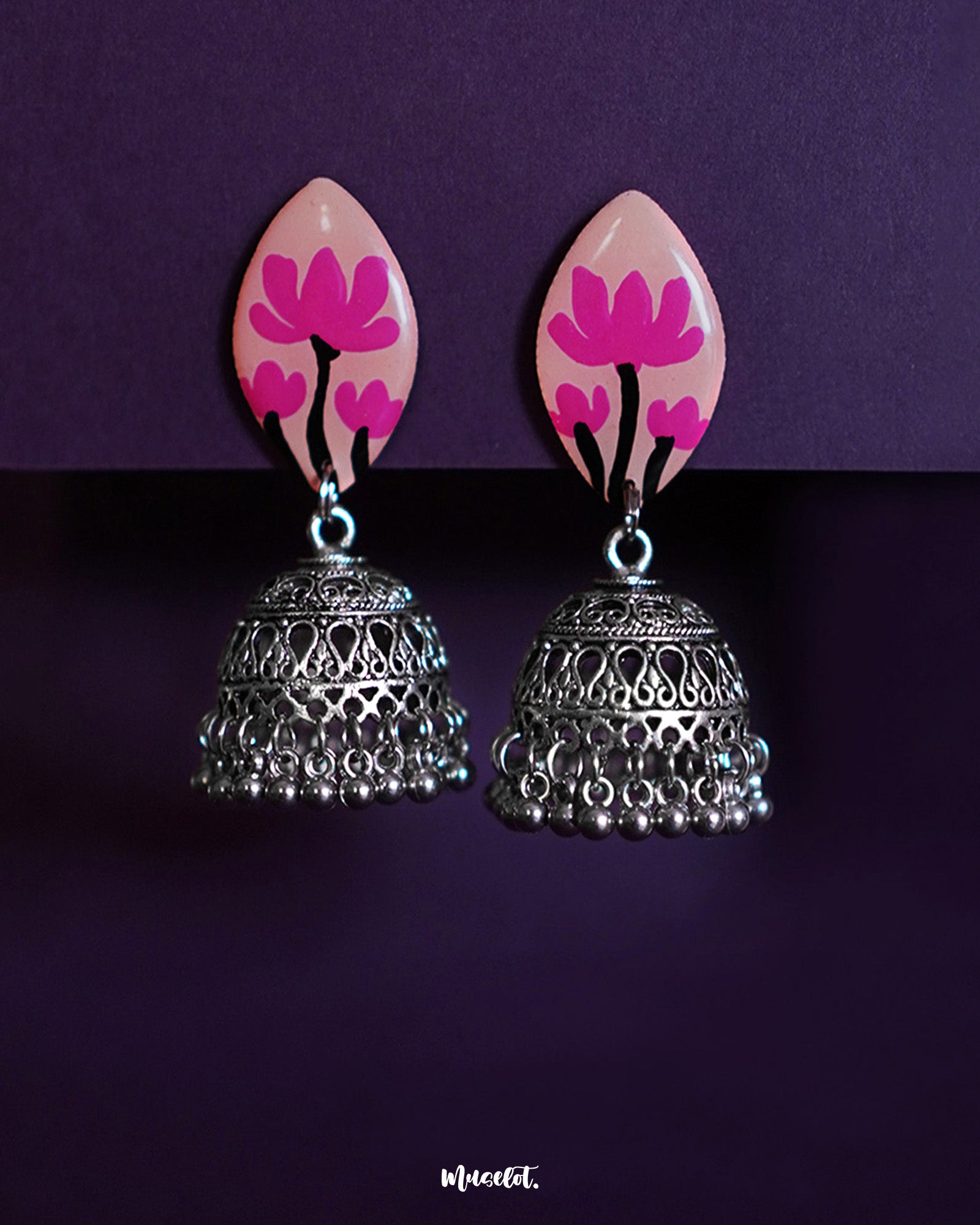 Kumudini jhumkas  handcrafted earrings featuring lotus-pink painted studs and oxidized silver dome-shaped jhumkas with intricate filigree and dangling ghungroos, displayed on a deep purple background-Muselot