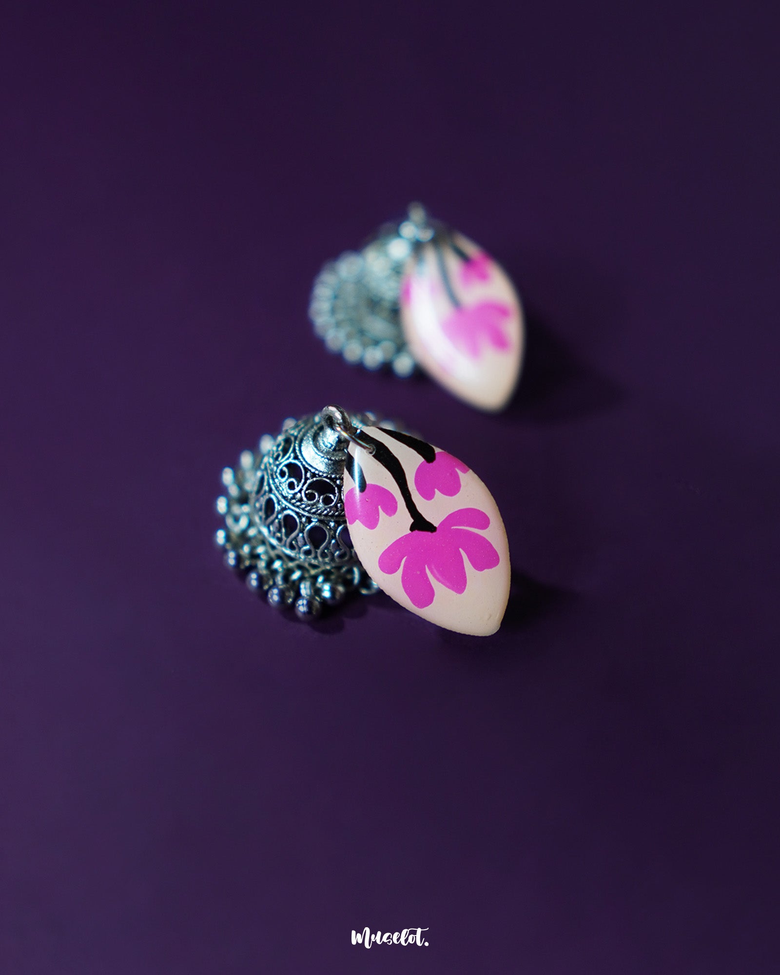 Close-up of Kumudini pink lotus jhumkas, showcasing intricate hand-painted petals and traditional craftsmanship with a soft backdrop – Muselot.