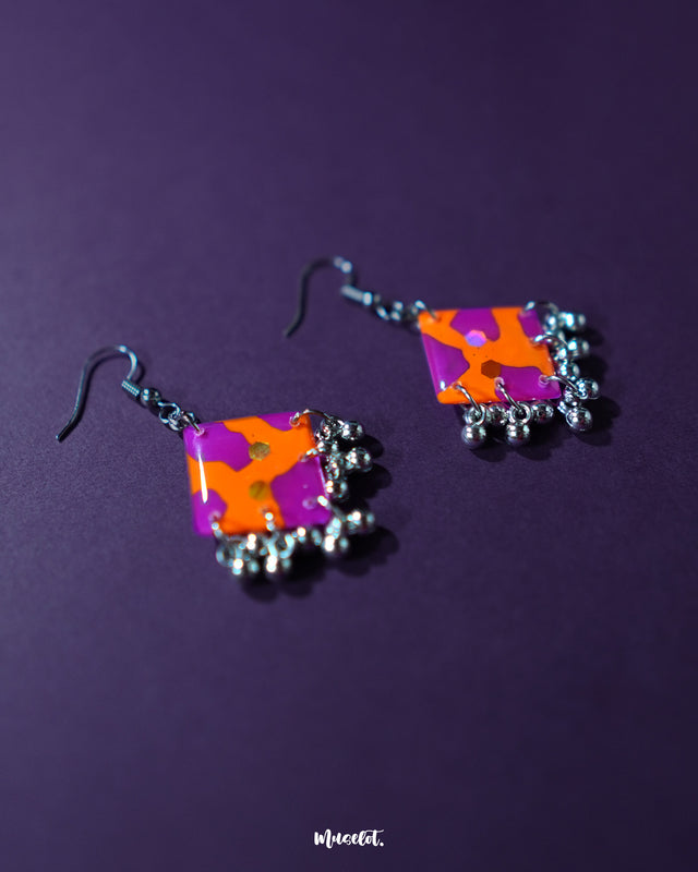 The Laalsavera hook earrings, featuring a sleek design and placed against a deep purple background, offer a sophisticated look — Muselot.
