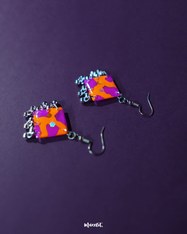 The Laalsavera earrings bring together bold design and graceful craftsmanship, with their elegance enhanced by the rich purple background — Muselot.