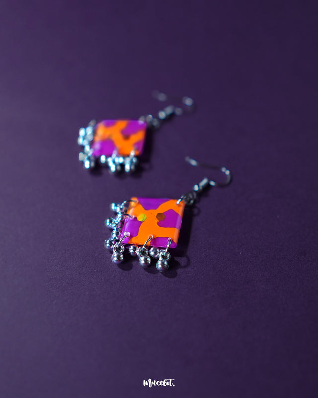 A captivating pair of Laalsavera hook earrings, resting elegantly with their abstract design standing out beautifully against a dark purple background — Muselot.