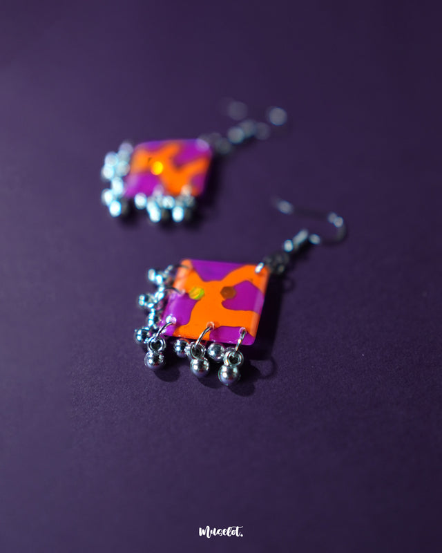 The Laalsavera hook earrings flaunt a unique artistic flair, with their bold, abstract shape highlighted perfectly against a moody purple background -Muselot.