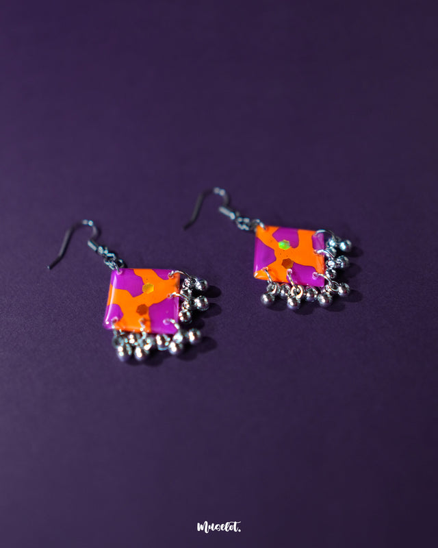 The Laalsavera hook earrings offer a striking design, beautifully highlighted against a deep purple background — Muselot.