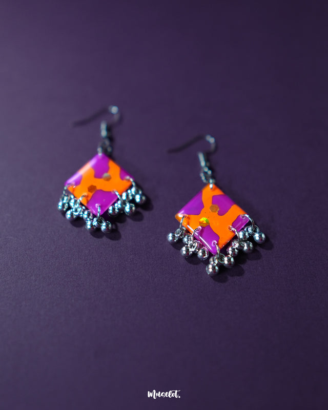 The Laalsavera hook earrings, showcased against a bold purple background, offer a stylish and contemporary touch — Muselot.