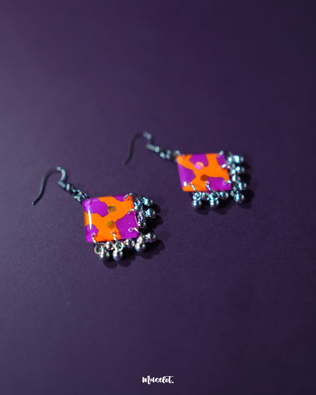 The Laalsavera hook earrings, elegantly displayed with a purple background, highlight their sleek design — Muselot.