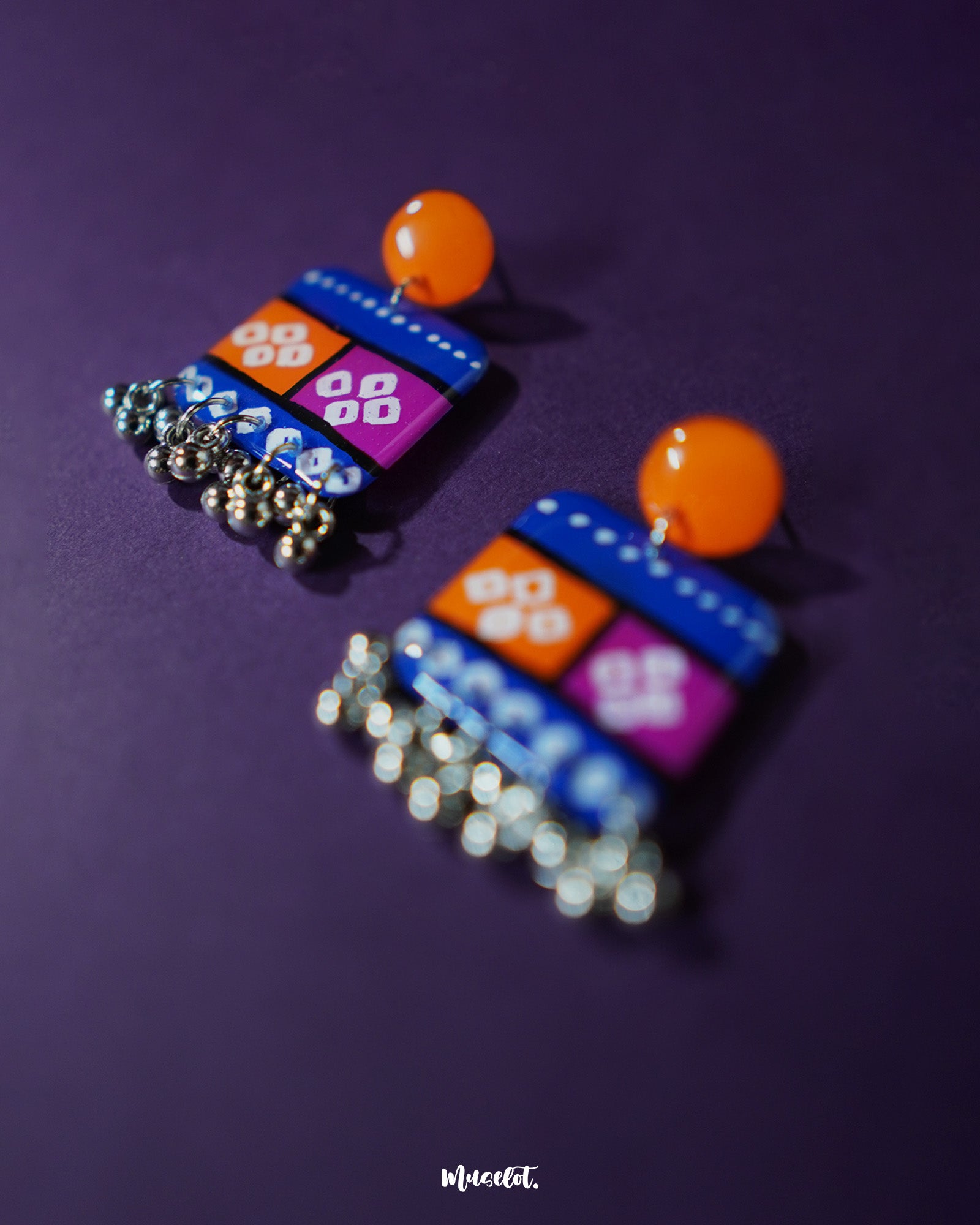 Zoomed-in view of the Leheriya traditional art drop earrings, featuring bright orange round studs connected to blue rectangular drops with orange and magenta blocks, adorned with white geometric patterns and dotted detailing, finished with dangling silver beads, highlighting their intricate handcrafted design – Muselot.