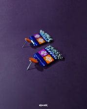 Leheriya traditional art drop earrings with bright orange round studs attached to blue rectangular drops featuring orange and magenta blocks, decorated with white geometric patterns and dotted detailing, finished with dangling silver beads, beautifully displayed to showcase their vibrant handcrafted charm – Muselot.
