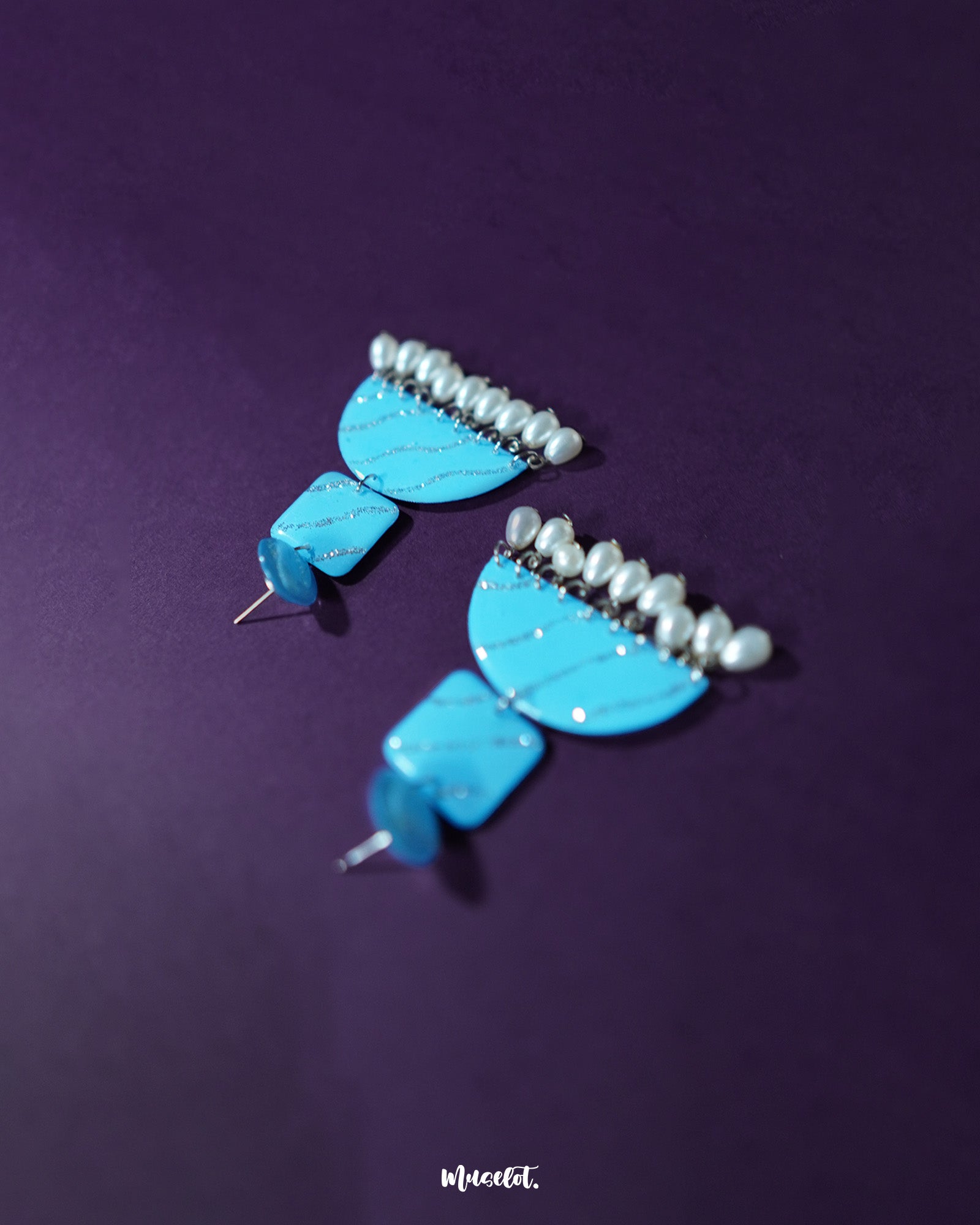 The Lehrbaan blue pearl jhumkas shine with a captivating blend of geometric elegance and traditional grace. The vibrant blue tone, kissed with silver shimmer, pairs effortlessly with the delicate pearls, creating a standout piece that’s perfect for those who love a modern take on ethnic accessories — Muselot.