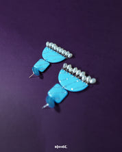 The Lehrbaan blue pearl jhumkas shine with a captivating blend of geometric elegance and traditional grace. The vibrant blue tone, kissed with silver shimmer, pairs effortlessly with the delicate pearls, creating a standout piece that’s perfect for those who love a modern take on ethnic accessories — Muselot.