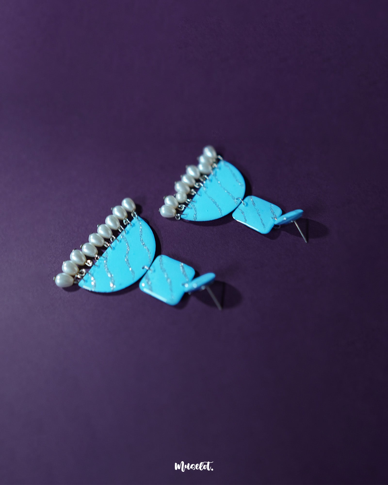 The Lehrbaan blue pearl jhumkas showcase a graceful silhouette as they dangle elegantly, with their vibrant blue domes and delicate pearl hangings exuding regal charm and festive allure — Muselot.