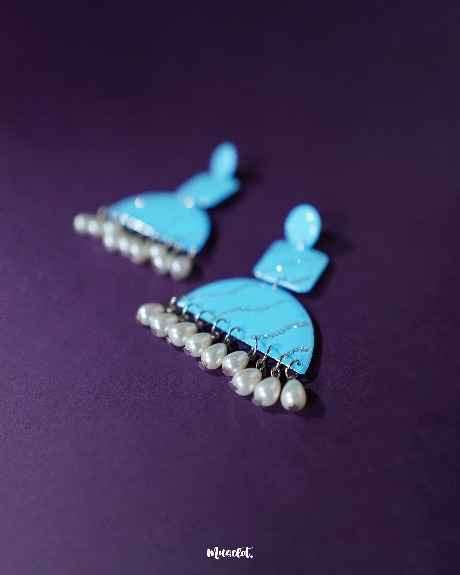 A close-up of the Lehrbaan blue pearl jhumkas reveals their enchanting craftsmanship — the deep blue enamelled domes are accentuated with glistening pearls and silver details, offering a sophisticated yet playful charm that beautifully bridges festive tradition and contemporary flair — Muselot.